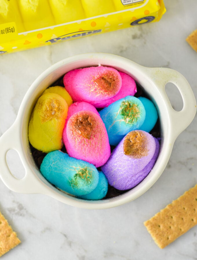 An oven safe container filled with festive Peeps S'mores Dip, with the colorful marshmallow chicks slightly golden brown from the oven.