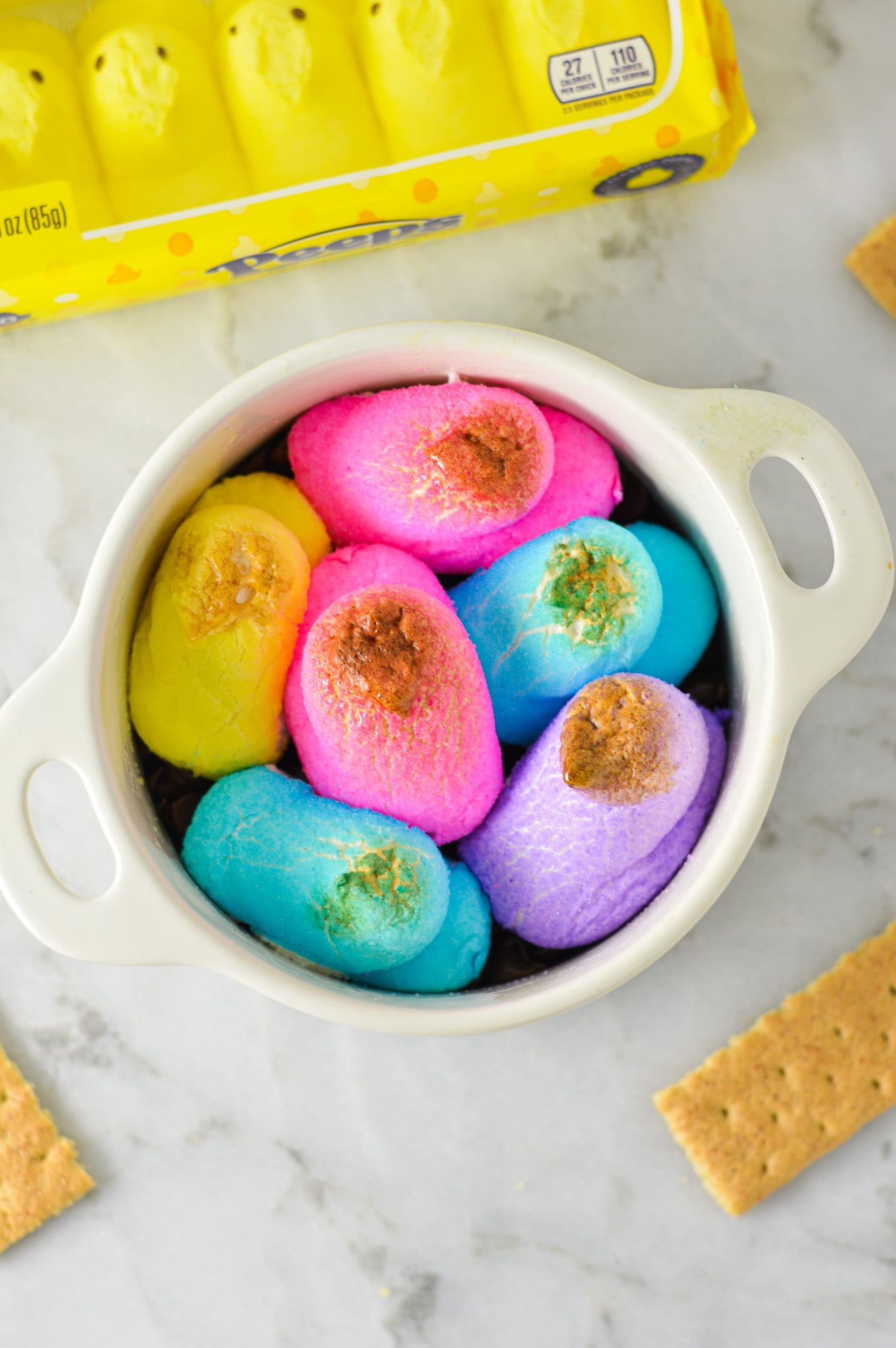 An oven safe container filled with festive Peeps S'mores Dip, with the colorful marshmallow chicks slightly golden brown from the oven.