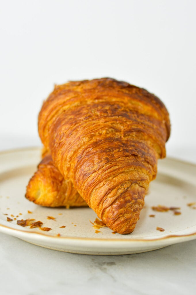 A buttery croissant made in the air fryer on a small plate, with croissant flakes littering the plate.