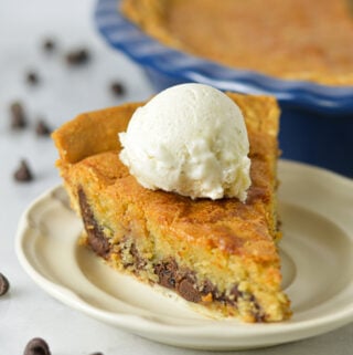 A slice of Chocolate Chip Cookie Pie on a small plate, with the whole pie in its ceramic pie pan in the background.