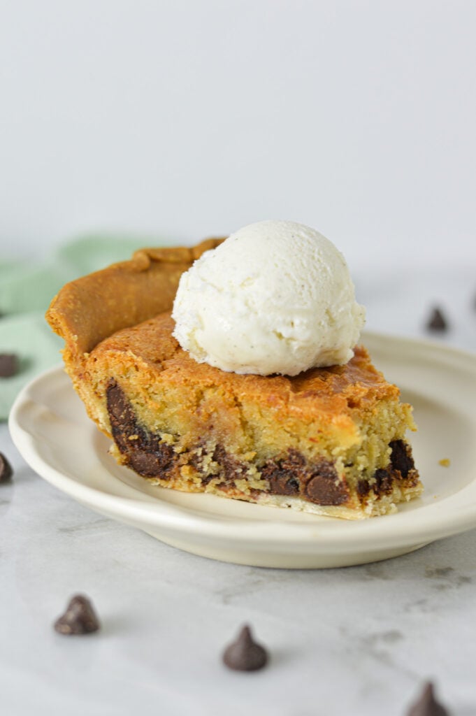 A slice of Chocolate Chip Cookie Pie, topped with a scoop of ice cream and stuffed with melty chocolate chips.