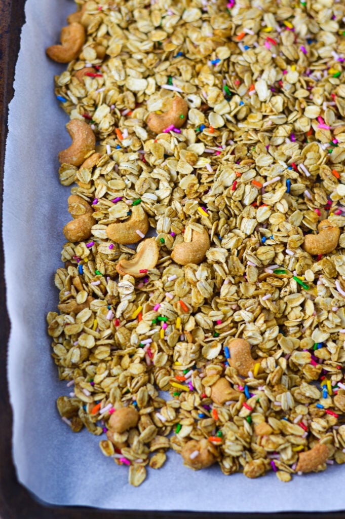 A parchment paper lined cookie sheet topped with golden brown Funfetti Granola.