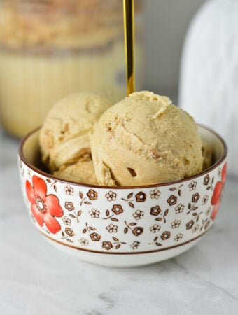 A small bowl of Ninja Creami Cinnamon Protein Ice Cream, with a Ninja Creami container in the background with some extra ice cream.