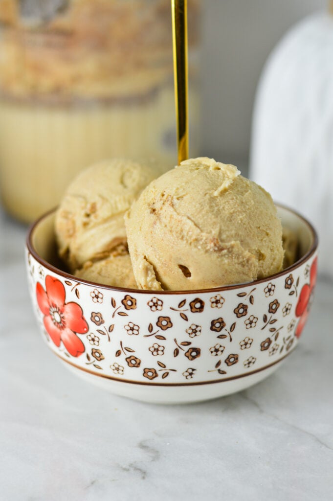 A small bowl of Ninja Creami Cinnamon Protein Ice Cream, with a Ninja Creami container in the background with some extra ice cream.