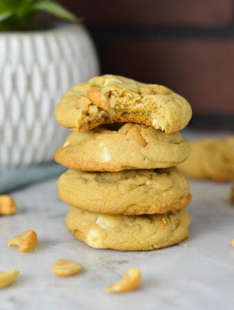 A stack of White Chocolate Cashew Cookies with a bite taken out of the top cookie showing the chewy texture.