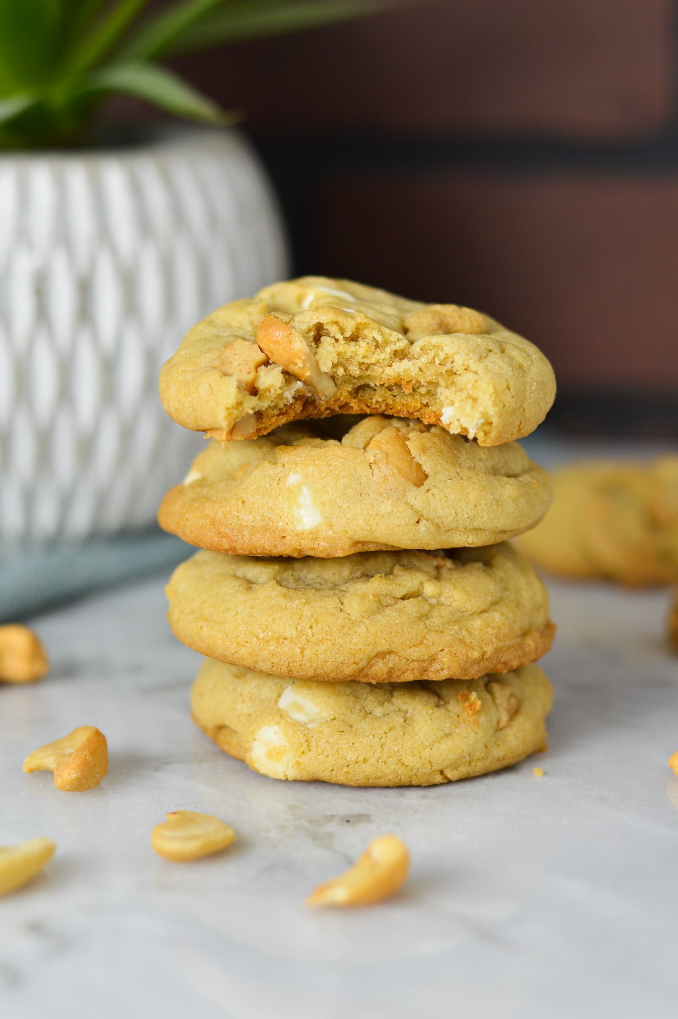 A stack of White Chocolate Cashew Cookies with a bite taken out of the top cookie showing the chewy texture.