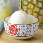 A small bowl full of Ninja Creami Pineapple Sorbet with a small spoon sticking out, showing the smooth texture of the ice cream.