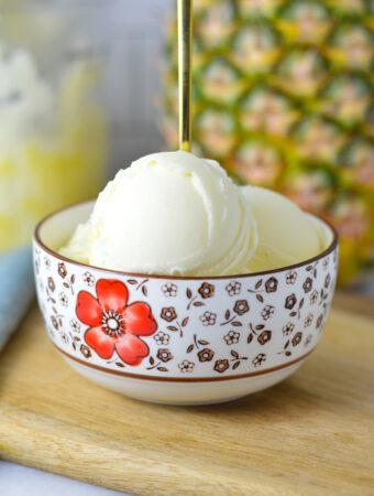 A small bowl full of Ninja Creami Pineapple Sorbet with a small spoon sticking out, showing the smooth texture of the ice cream.