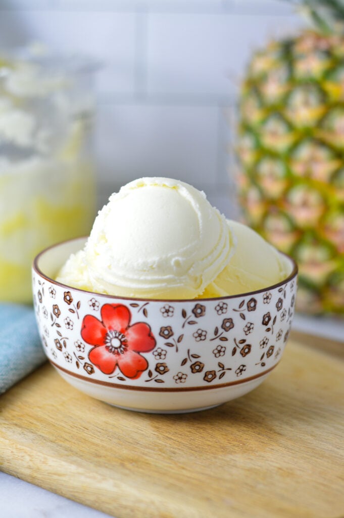 A bowl of Ninja Creami Pineapple Sorbet with a Ninja Creami container in the background filled with the leftover sorbet.