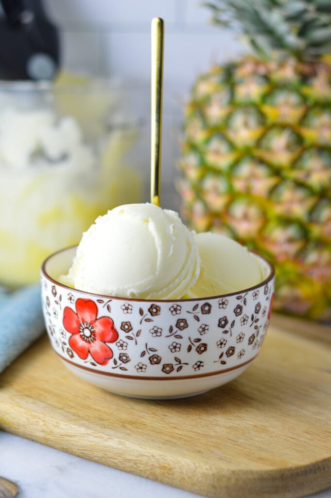 A small bowl of Pineapple Sorbet made in the Ninja Creami machine, with a whole pineapple in the background.