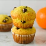 A stack of Orange Chocolate Chip Muffins, with a fresh orange in the background.