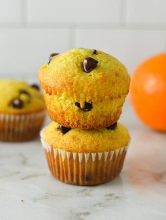 A stack of Orange Chocolate Chip Muffins, with a fresh orange in the background.