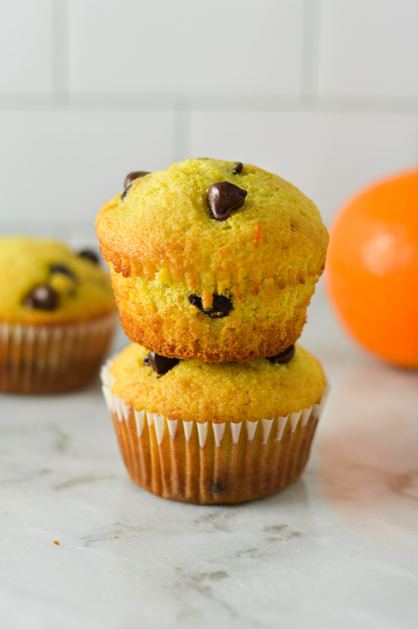 A stack of Orange Chocolate Chip Muffins, with a fresh orange in the background.