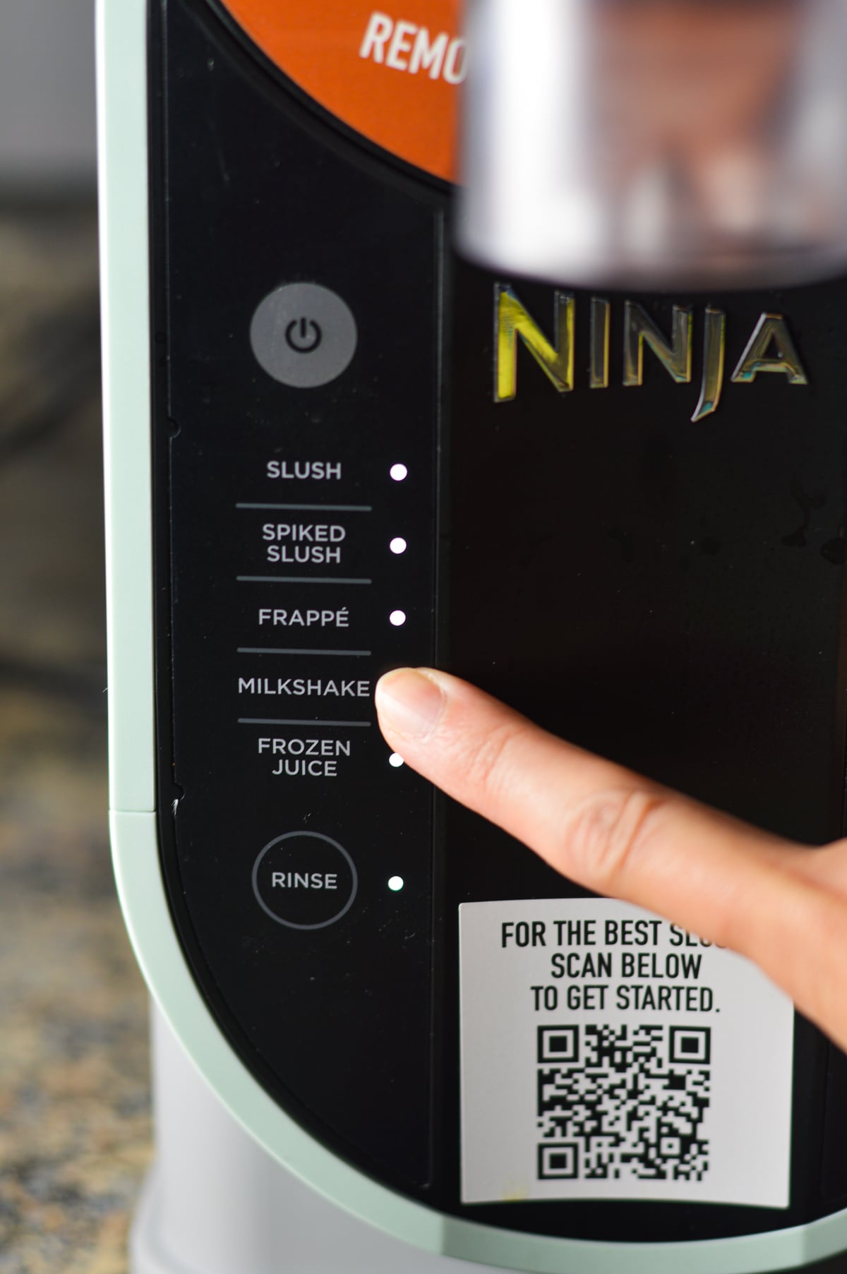A finger selecting the Milkshake preset on the Ninja Slushi machine.