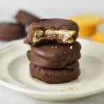 Stack of three chocolate-covered Nutella Ritz cracker sandwiches on a white plate, with a bite taken out of the top cracker showing the Nutella filling.