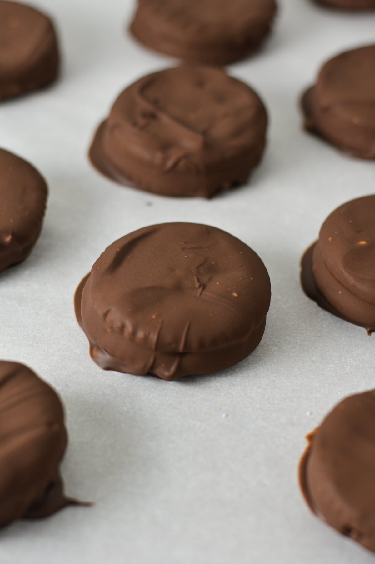 Close-up of fully set, chocolate-coated Ritz cracker sandwiches resting on parchment paper.