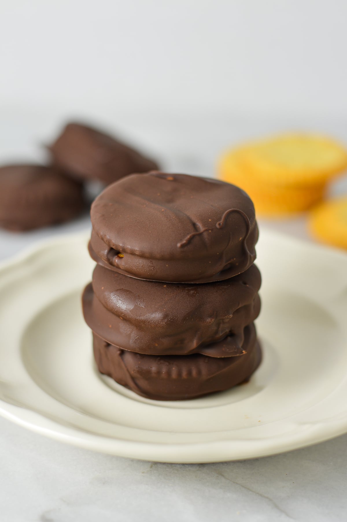 Stack of three chocolate-covered Nutella Ritz cracker sandwiches stacked vertically on a white plate.