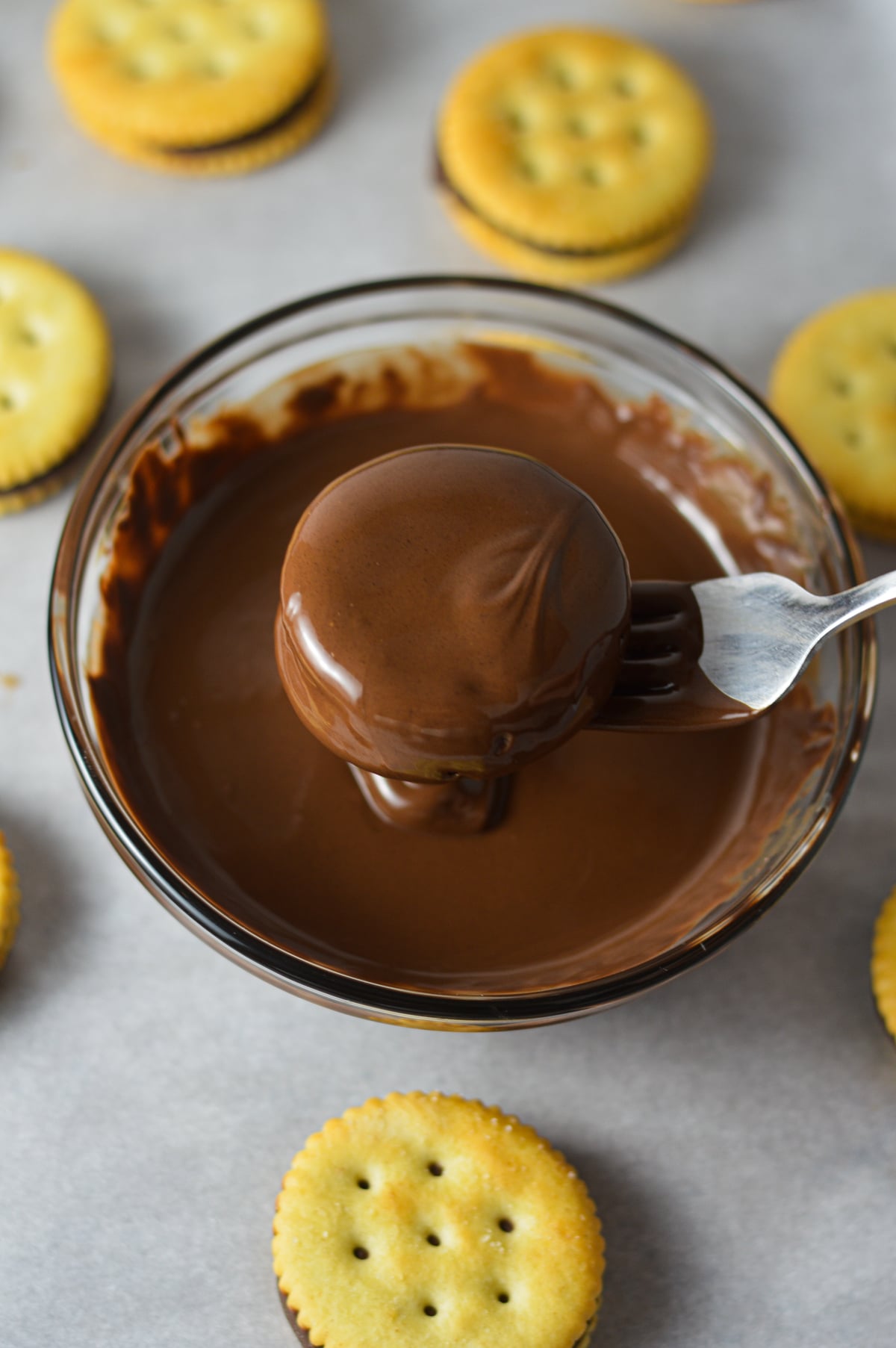 Dipping a Nutella-filled Ritz cracker sandwich into a small glass bowl of melted chocolate using a fork.