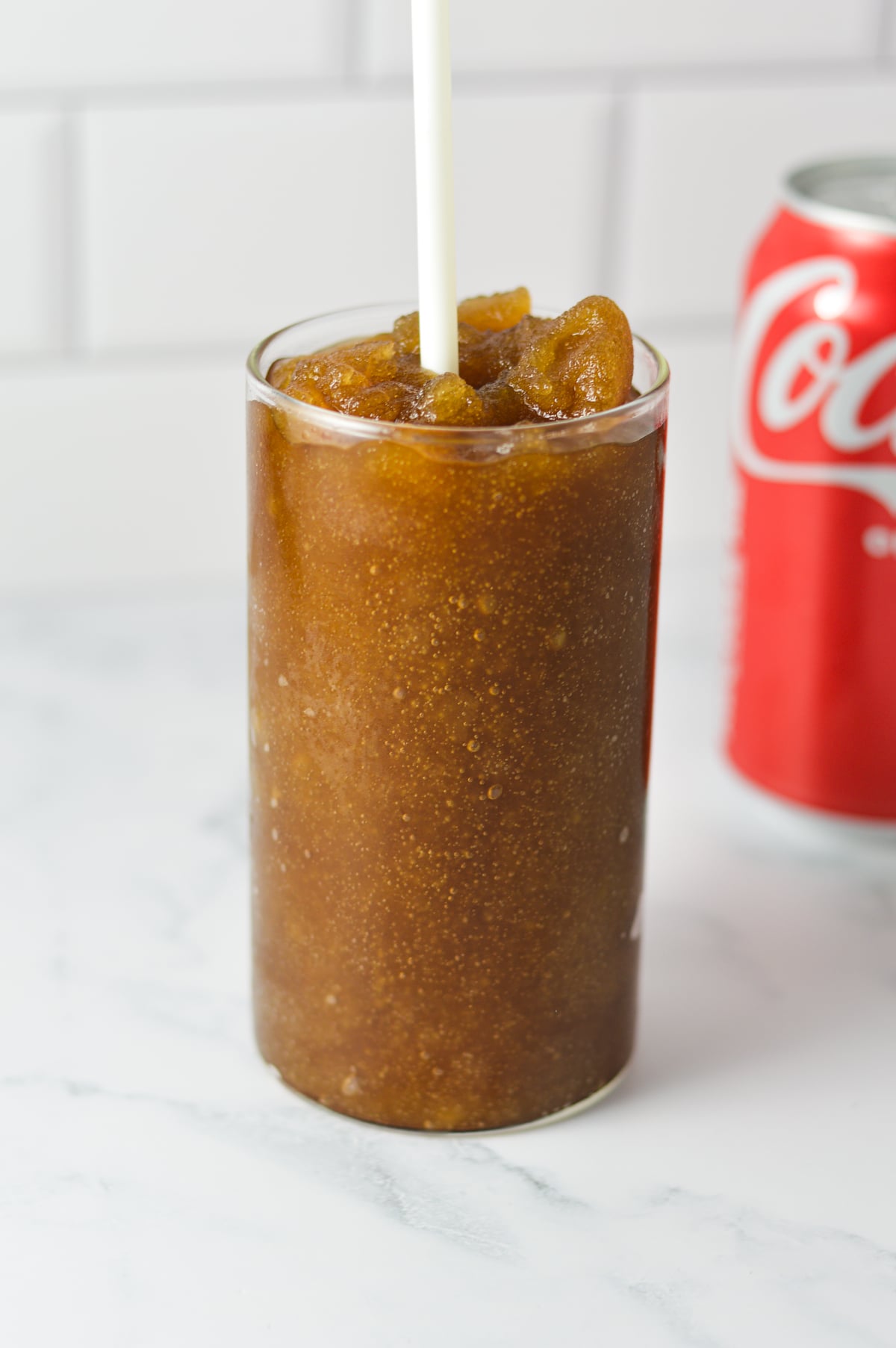 A tall glass filled with Ninja Slushi Rum and Coke with a white straw in it, showing the slushie texture of the cold drink.