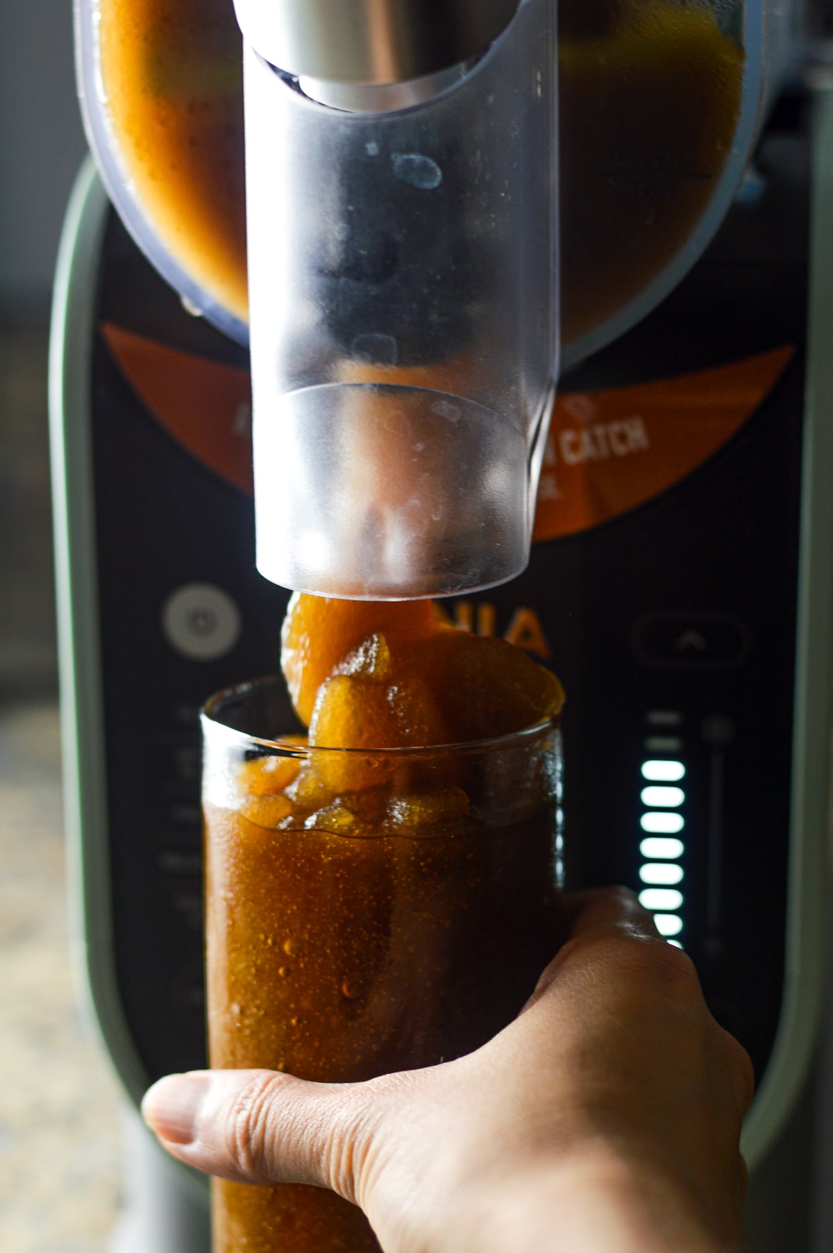 The Ninja Slushi machine dispensing a perfectly slushed Ninja Slushi Rum and Coke into a tall glass cup.