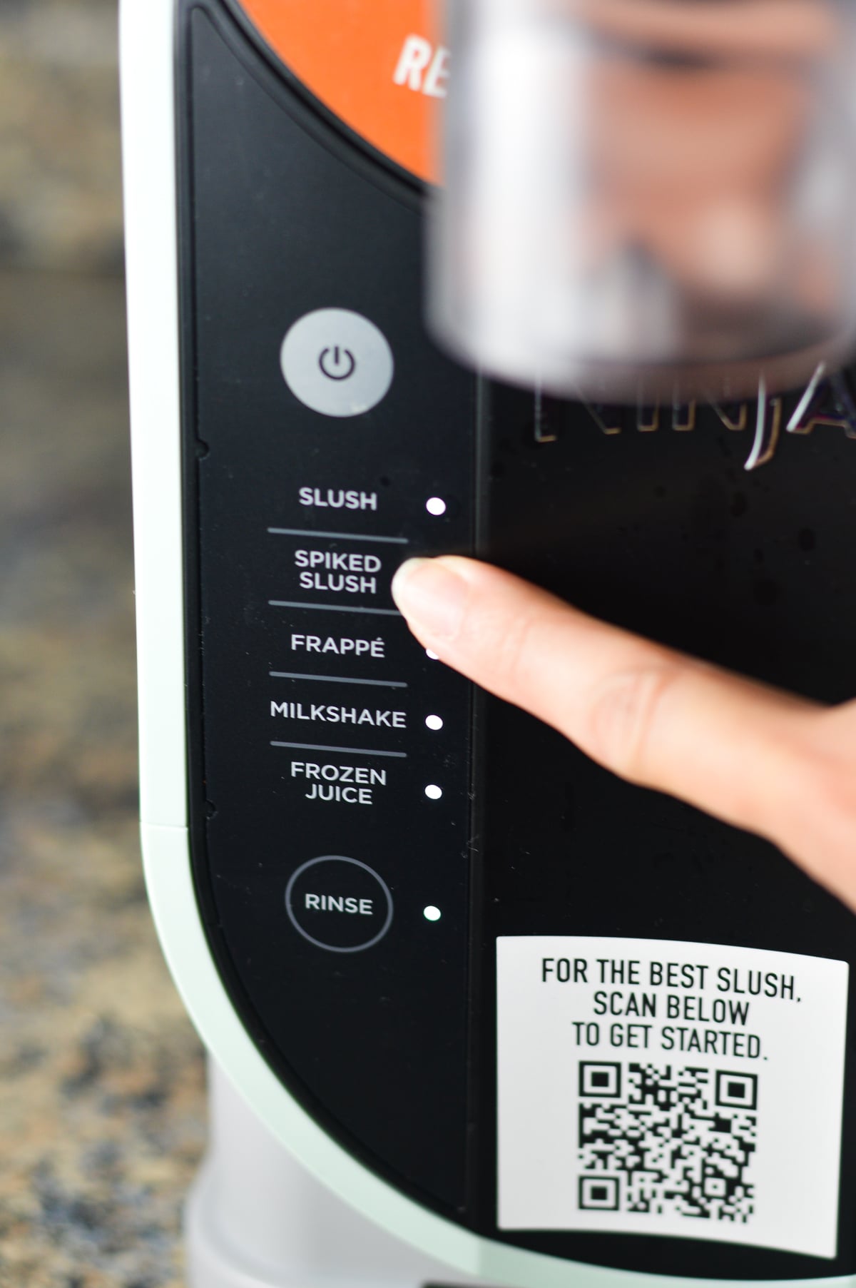 A finger pressing the Spiked Slush preset on the Ninja Slushi machine.