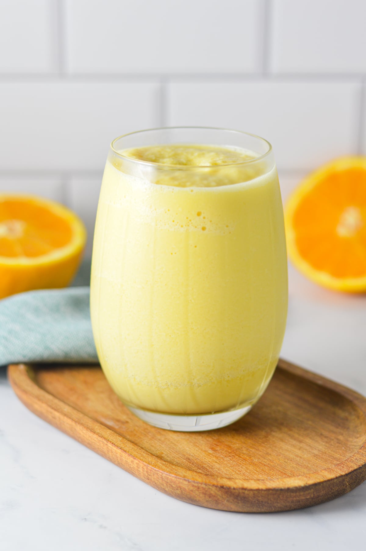 A creamy Ninja Slushi Orange Julius served in a glass on a wooden board with orange slices in the background.
