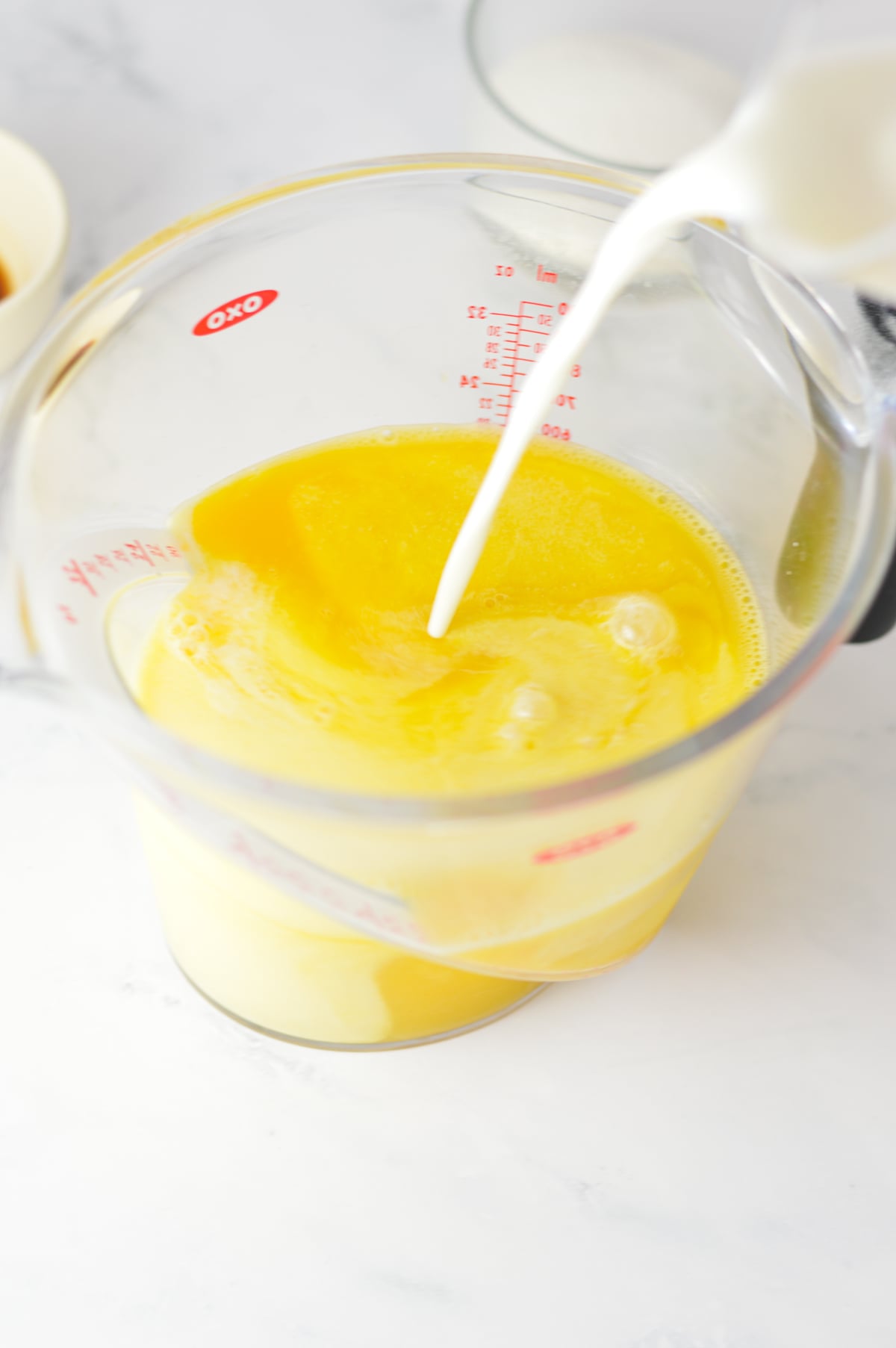 Half and half cream being poured into a large liquid measuring cup filled with orange juice.