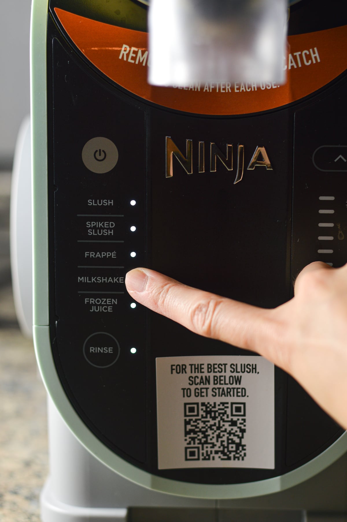 A finger pressing the milkshake preset on the Ninja Slushi machine.