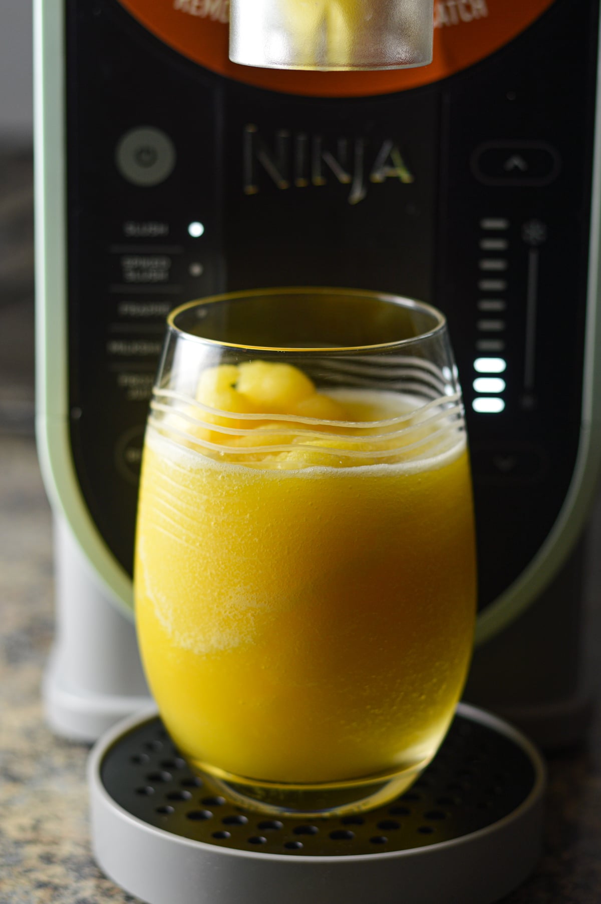 A glass of a slushy Virgin mimosa sitting in front of a Ninja Slushi machine.