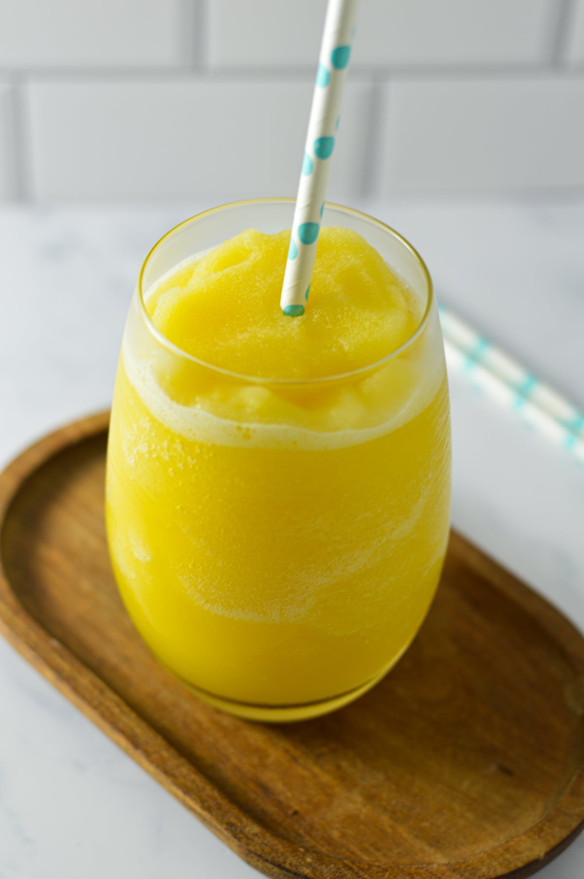 A clear glass filled with a slushy orange virgin mimosa and a paper straw, resting on a wooden surface.