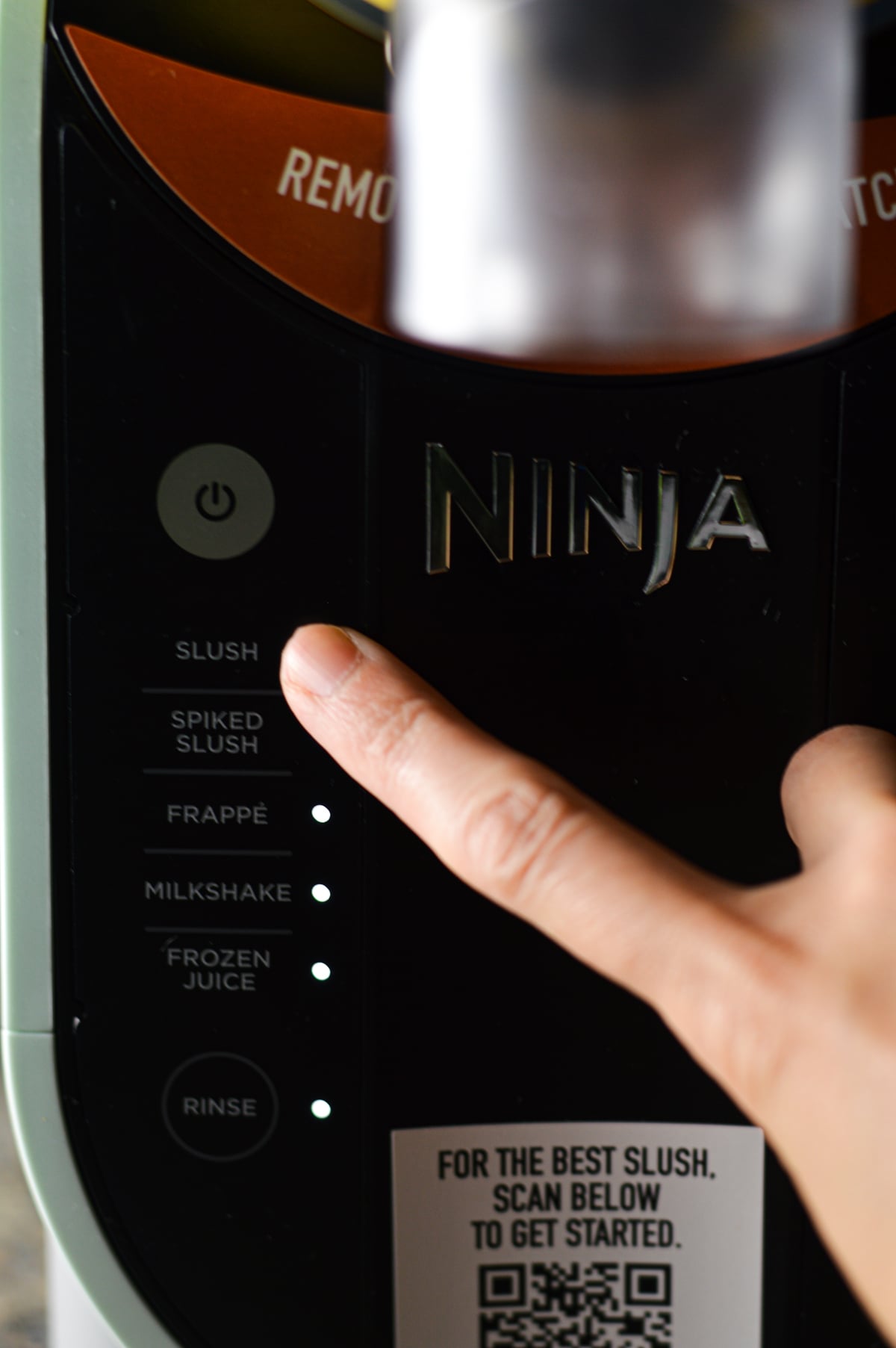 A finger pressing the Slush preset on the Ninja Slushi drink machine.