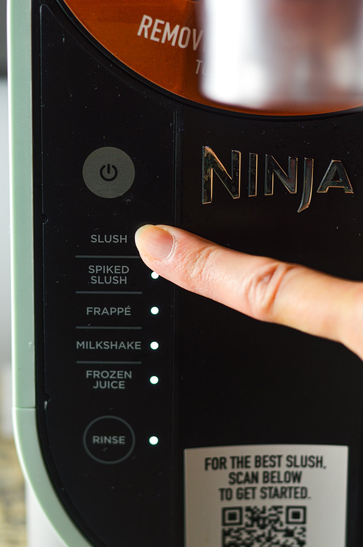 A finger pressing the SLUSH button on the Ninja Slushi machine.