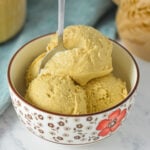 Scoops of creamy coffee ice cream in a bowl with a spoon resting inside, set against a warm, rustic background.