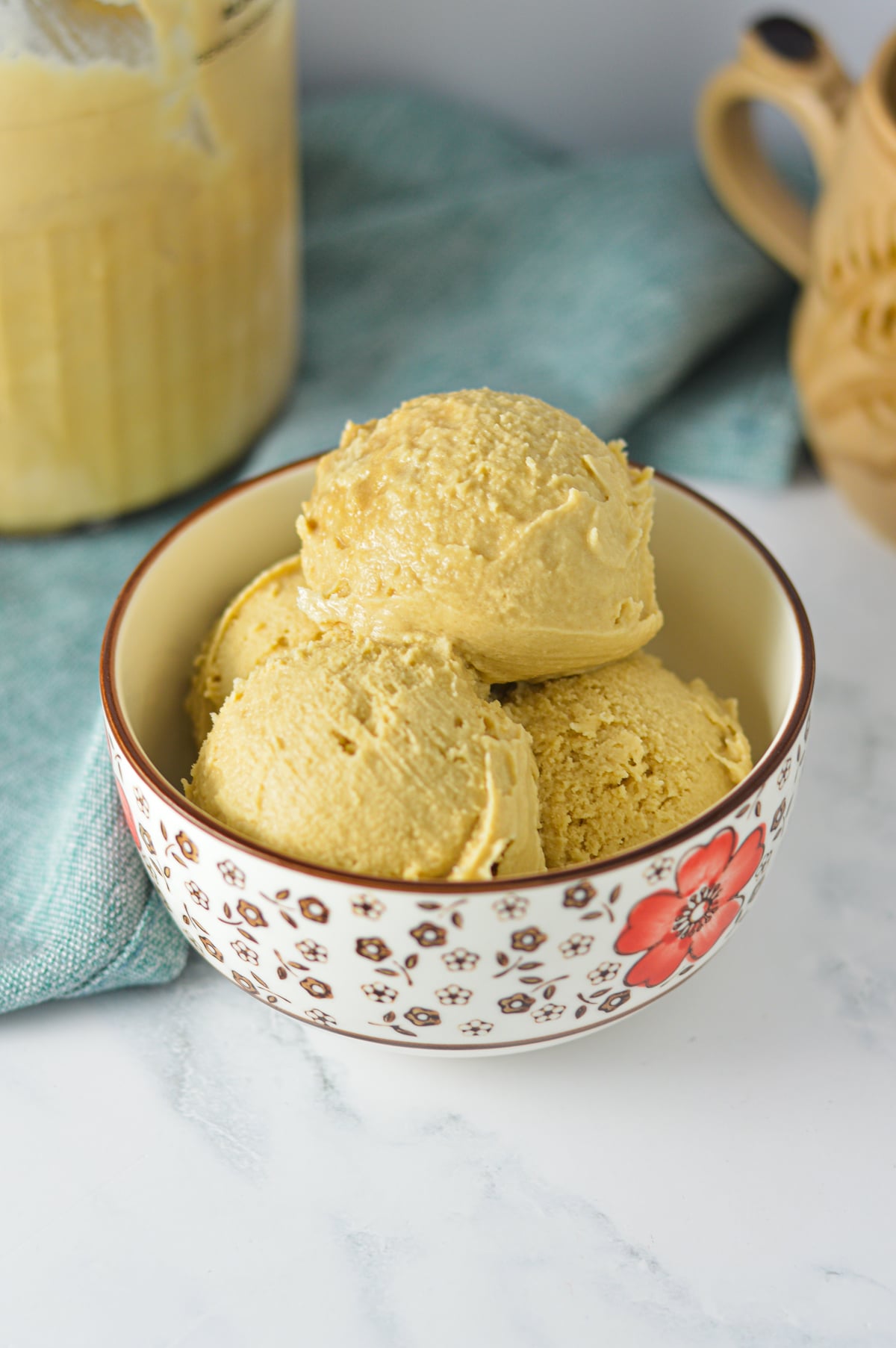 Scoops of creamy coffee ice cream served in a floral patterned bowl with a spoon, set against a warm and cozy background.