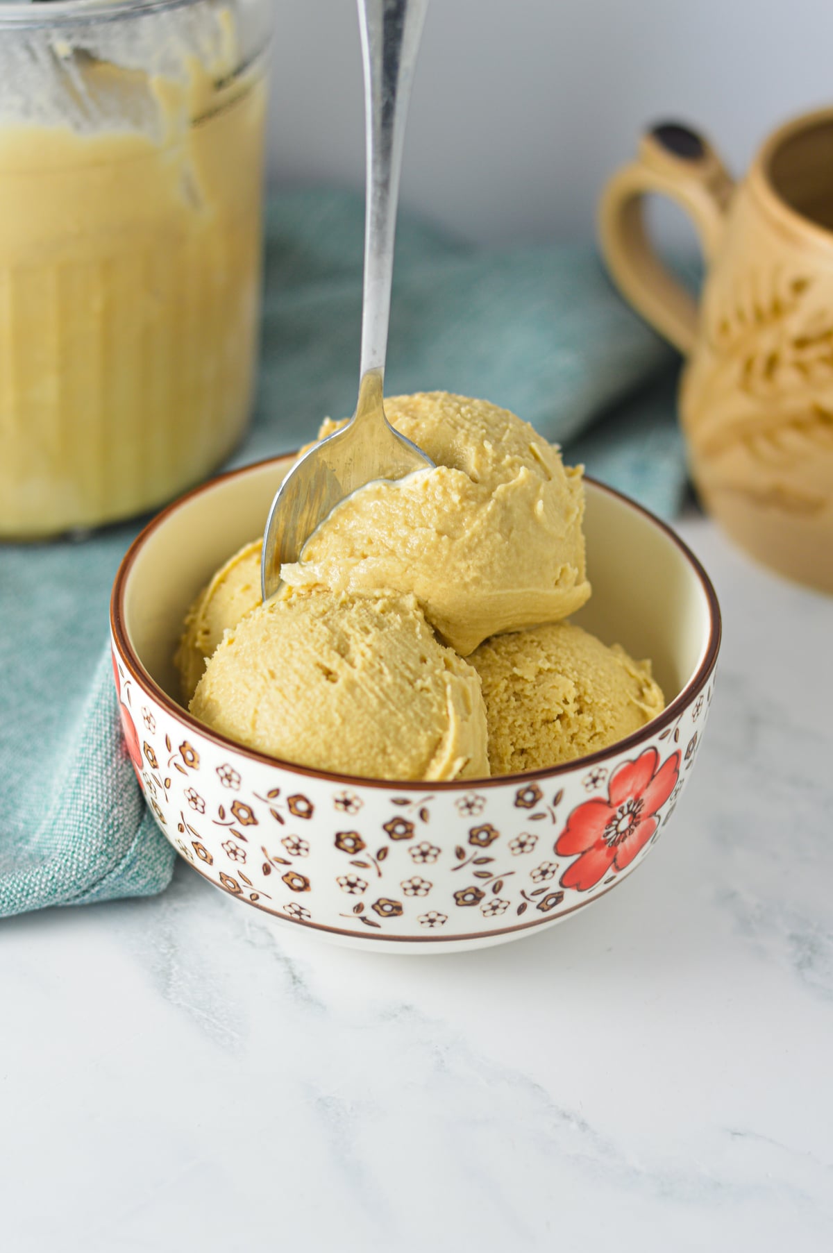 Scoops of creamy coffee ice cream served in a floral patterned bowl with a spoon, set against a warm and cozy background.