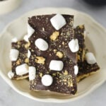 S'mores Chocolate Bark topped with mini marshmallows and graham cracker crumbs on a white plate.