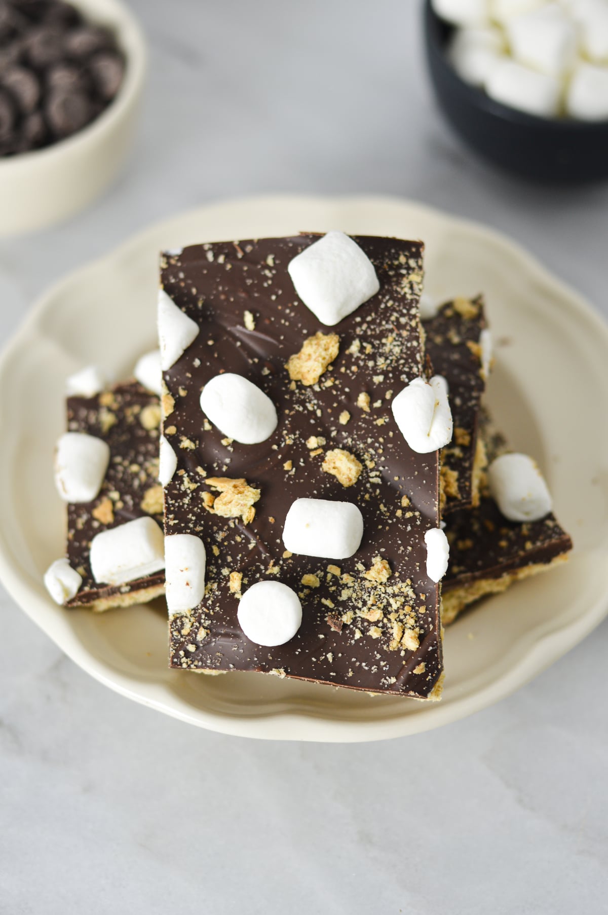 S'mores Chocolate Bark topped with mini marshmallows and graham cracker crumbs on a white plate.